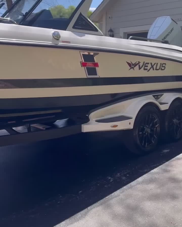 Vexus bass boat on its trailer in a driveway, hull and trolling motor visible