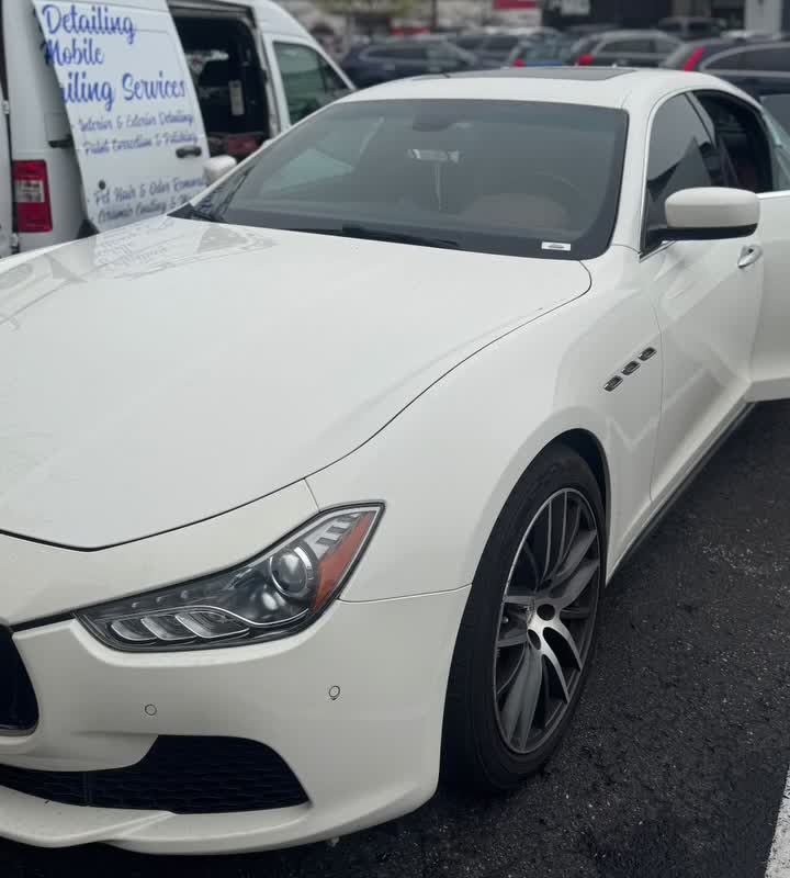 White Maserati Ghibli parked beside the mobile detailing van at a work lot